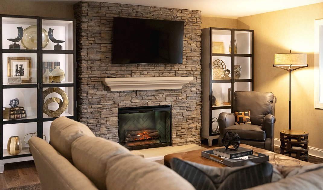 A warm living room with a stacked-stone fireplace and layered seating by JK Home Design