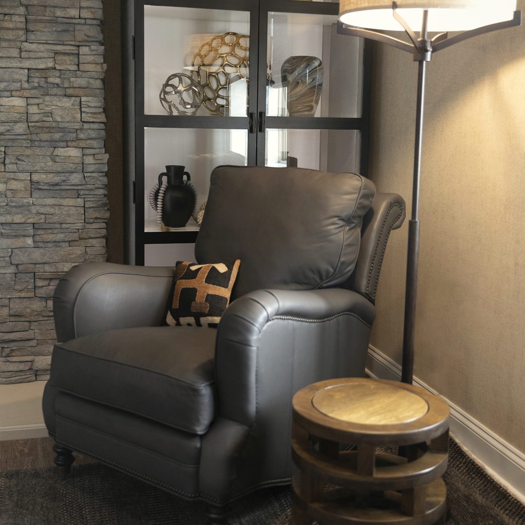 Den with a grey leather recliner, a log side table and a stacked-stone accent wall