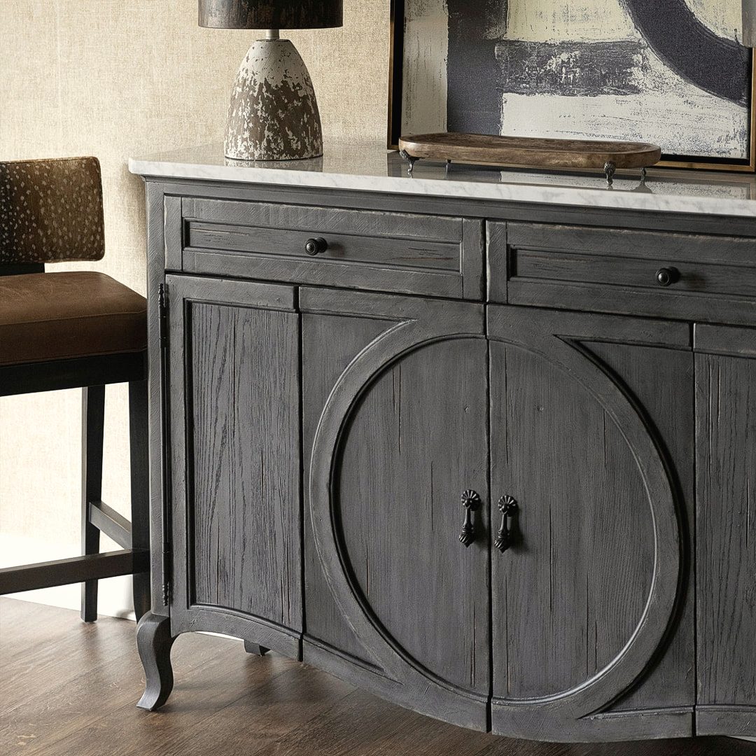 Grey storage cabinet with a circular carved door detail styled with greenery