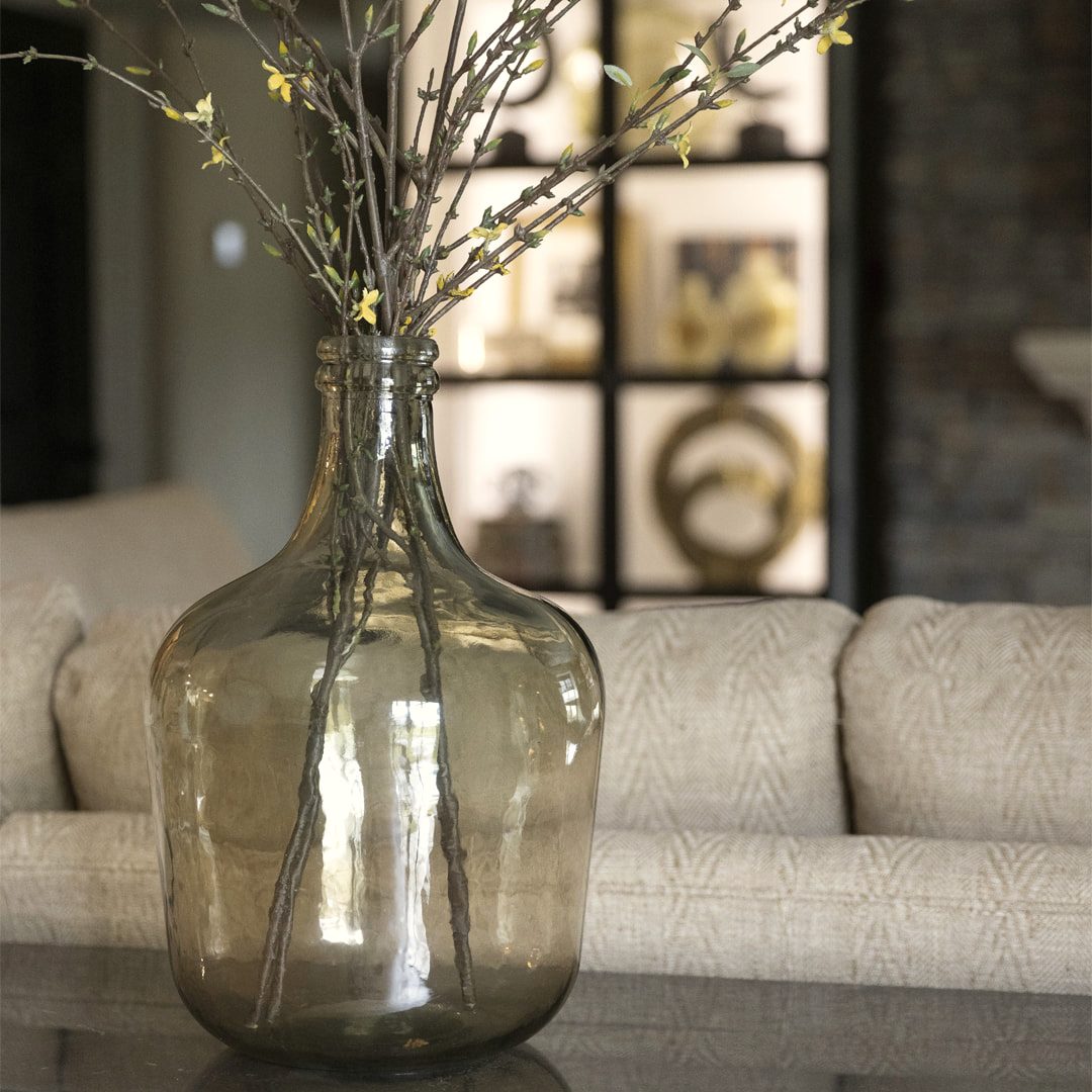 Oversized glass demijohn vase styled with bare branches as a floor accent
