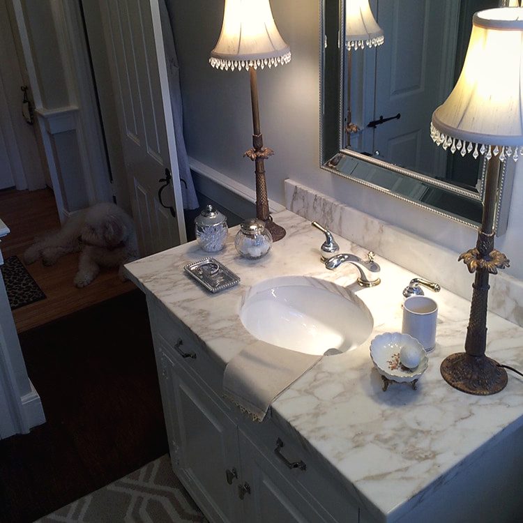 Bathroom vanity with a framed mirror, paired table lamps and a marble counter