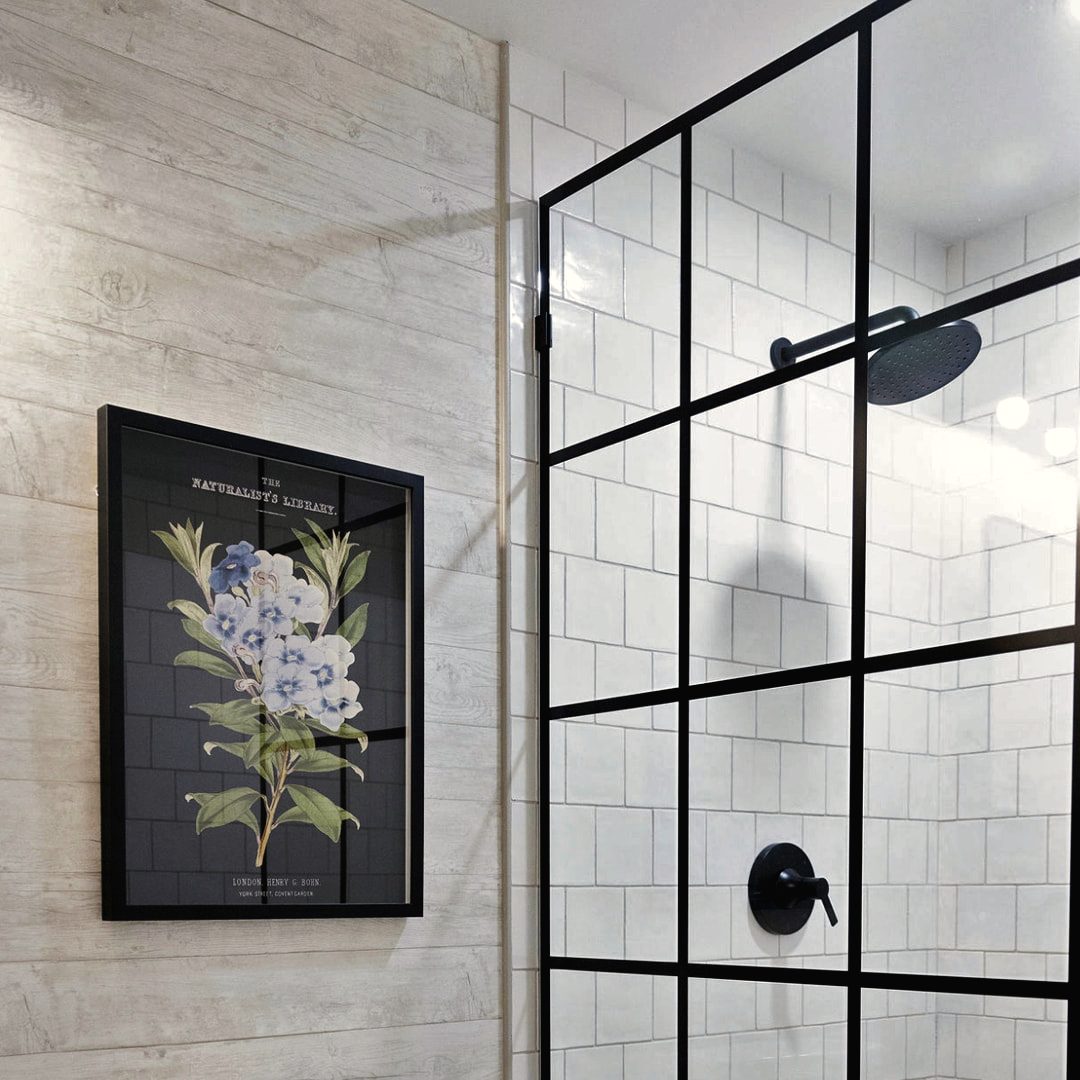 Bathroom with a black-framed glass shower, subway tile and framed botanical art