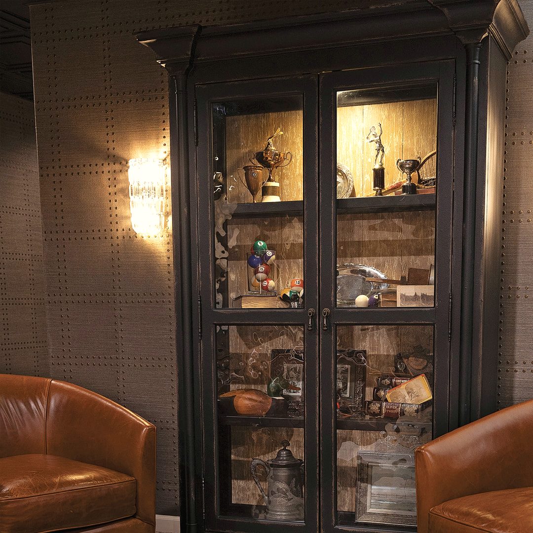 Illuminated glass display cabinet filled with collected objects beside a leather chair
