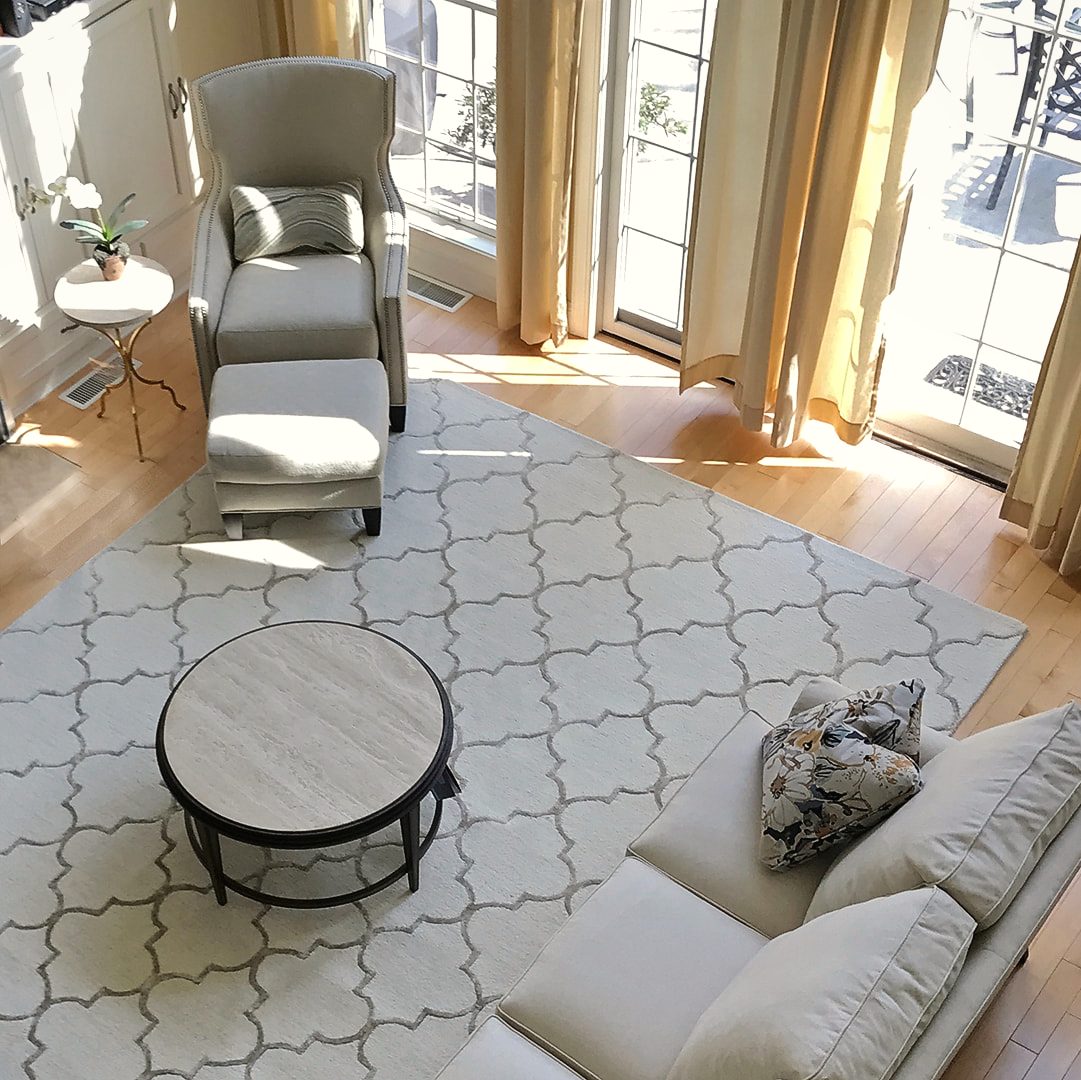Living room with white wing chairs, a patterned area rug and floor-length drapery