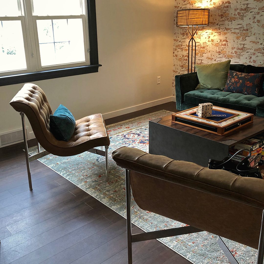 Living room with a leather lounge chair, a green velvet chair and a low ottoman