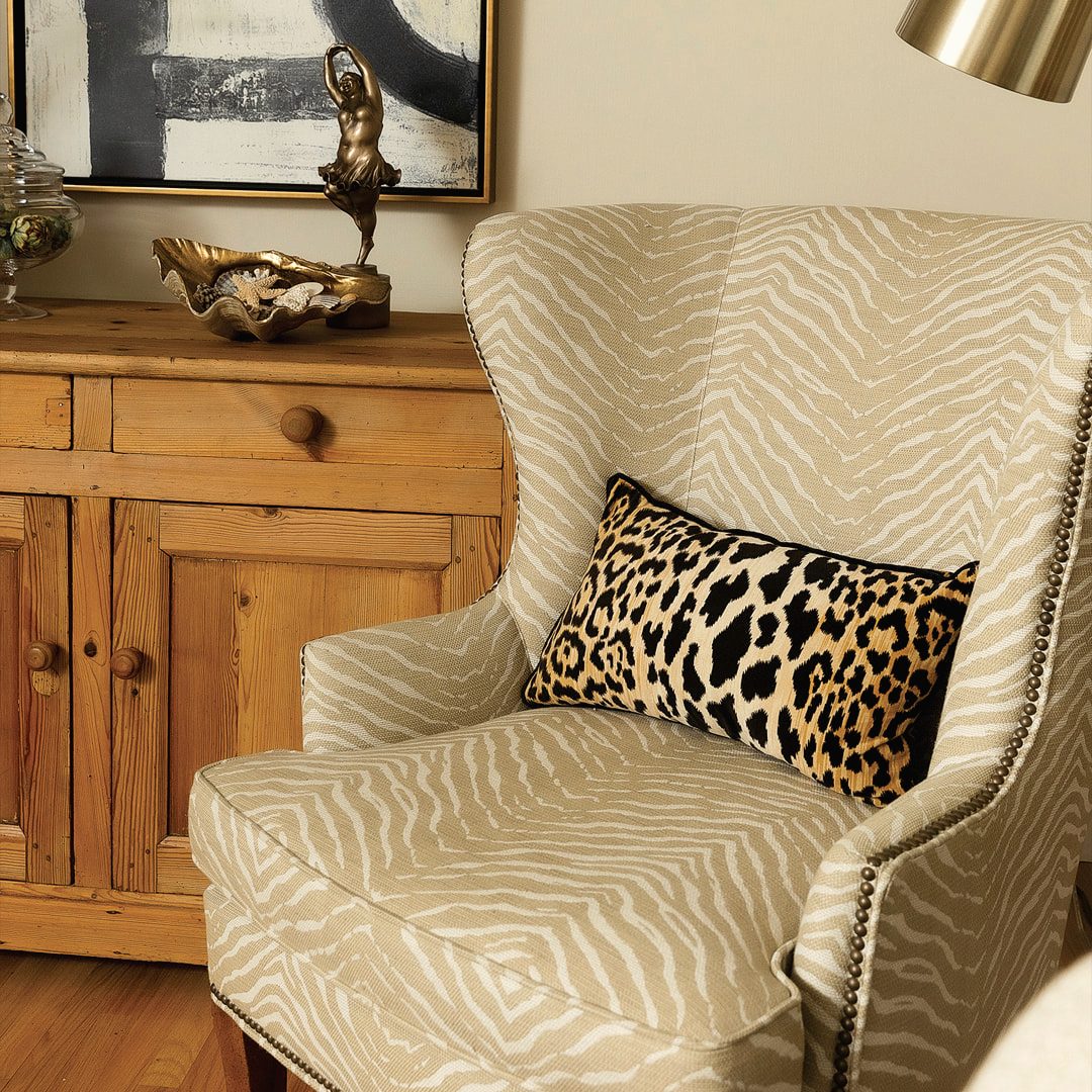 Cream wingback chair dressed with a leopard-print pillow beside a pine cabinet