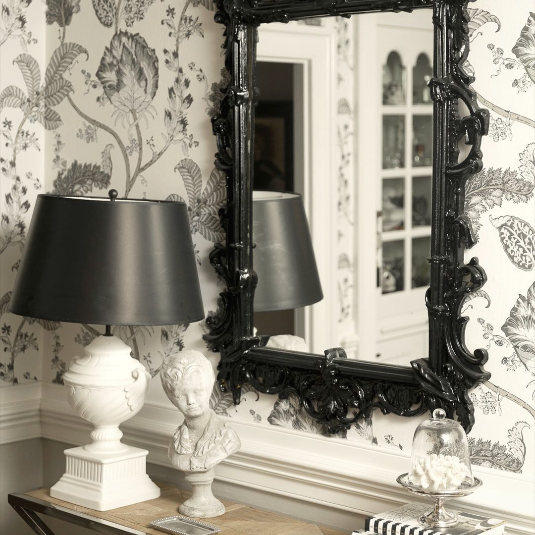 Console vignette with an ornate black mirror, a lamp and floral wallpaper
